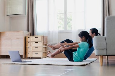 Asyalı genç anne ve kızı evde esneme egzersizi yoga yapıyorlar. Ebeveyn-öğretim çocuğu her gün düzenli olarak fiziksel sağlık ve refahı korumak için çalışmalıdır..