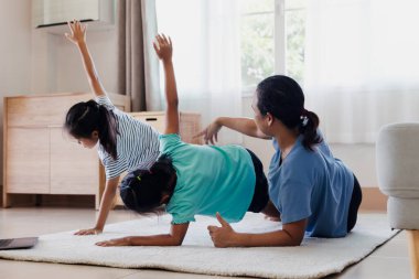 Asyalı genç anne ve kızları evde birlikte egzersiz yogası yapıyorlar. Ebeveynler ve çocuklar her gün düzenli olarak fiziksel sağlık ve refahı korumak için güçlü olmaya çalışırlar..