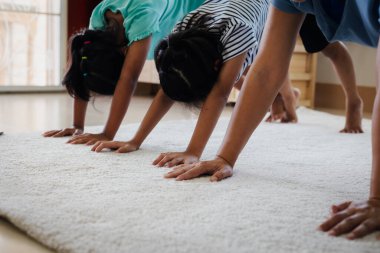 Asyalı genç anne ve kızları evde birlikte egzersiz yogası yapıyorlar. Ebeveynler ve çocuklar her gün düzenli olarak fiziksel sağlık ve refahı korumak için güçlü olmaya çalışırlar..