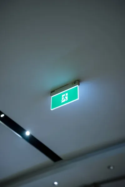 green emergency exit or fire exit hanging sign showing the way to escape from building of hospital or hotel at night time, shallow depth of field