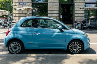 A blue tiny Fiat 500 parked by street in Zurich city.  Fiat 500 is a compact city car built by Italian automaker.