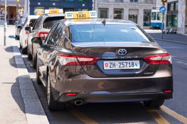 Brown Toyota Camry Hybrid as a Taxi car, Taxi drivers in Switzerland are allowed to drive any road vehicle under licence as a taxi. No set colour to a taxi.