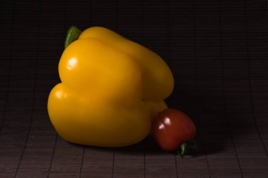 Konu fotoğrafçılık: Küçük kırmızı bir kiraz domatesi ve siyah bir hasırın üzerindeki büyük sarı kırmızı biber..