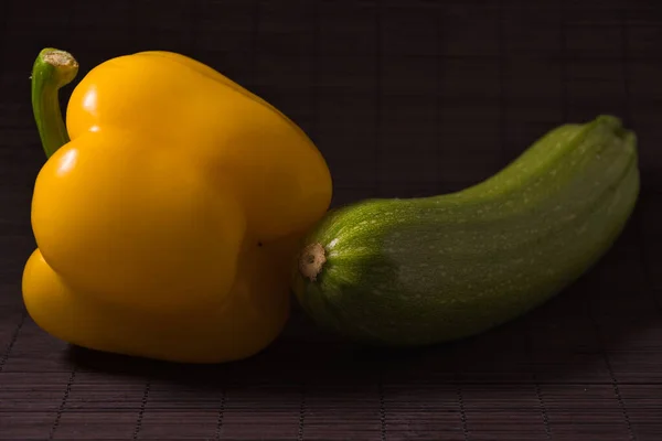 Konu fotoğrafçılığı: Siyah bir hasırın üzerinde sarı biber ve yeşil kabak yakın plan..