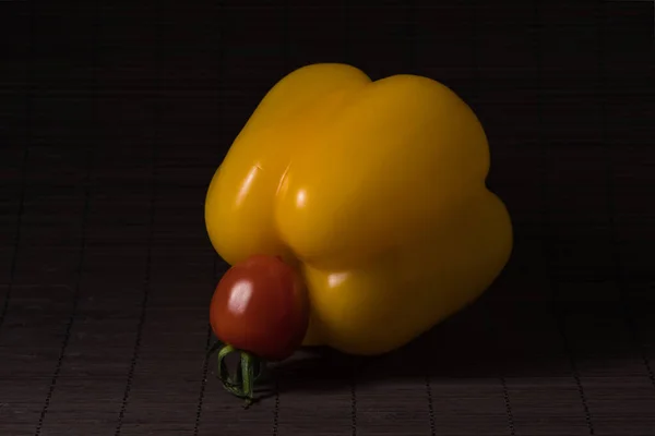 Konu fotoğrafçılığı: Siyah bir hasırın üzerinde sarı paprika ve kırmızı kiraz domatesi yakın çekim.