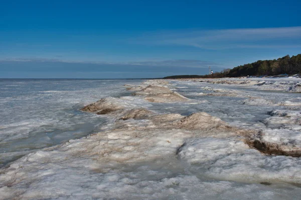 Baharın başlarında Baltık Denizi kıyıları, güneşli bir günde açık bulutlu mavi gökyüzünün altında gri, yumuşak ve kirli kar..