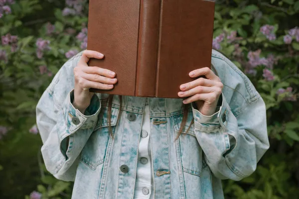 Fotografía sin rostro de una mujer sosteniendo un libro frente a su cara al aire libre — Foto de Stock