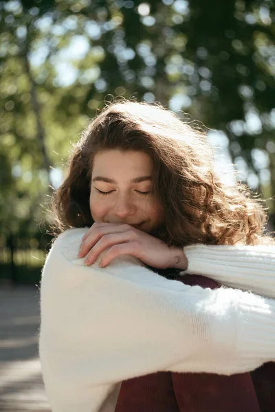 Mujer morena sonriente con los ojos cerrados sentada en el parque — Foto de Stock