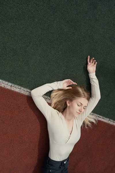 Joven rubia acostada en un campo deportivo de backetball con los ojos cerrados — Foto de Stock