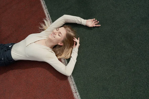 Young smiling blonde female lying on a backetball sport field Stock Picture