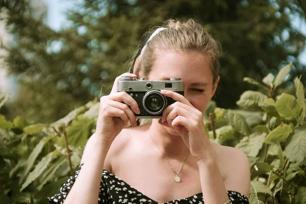 Young blonde female holding focusing vintage film camera outdoors Stock Photo
