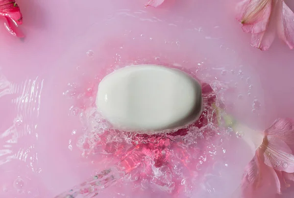 분홍빛 물에 꽃을 튀기며 몸을 돌보는 하얀 비누, — 스톡 사진