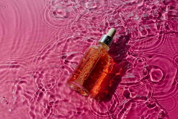 Suero narutal de vitamina en una botella de vidrio en agua rodeada de rosa Fotos De Stock Sin Royalties Gratis