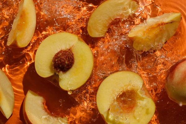 Cut peaches with splashing water on orange Royalty Free Stock Photos