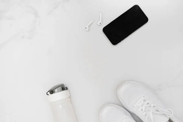 Vue du dessus des baskets, bouteille d'eau, smartphone avec écouteurs sur fond blanc. — Photo