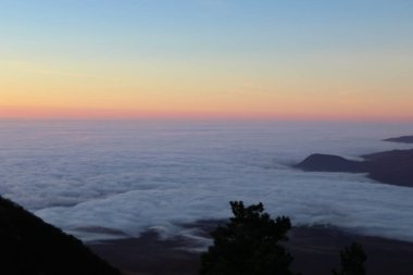 Dağlarda yükselen güneşin manzarası. Vadideki bulutların üzerinde güneşten gelen kırmızı refleksler. Gerçek görünüm