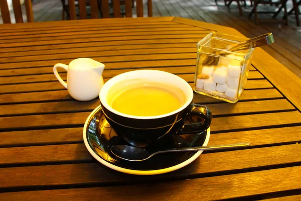 Kahverengi ahşap bir masanın üzerinde bir fincan taze demlenmiş kahve. Süt kabı ve şeker kasesi. 