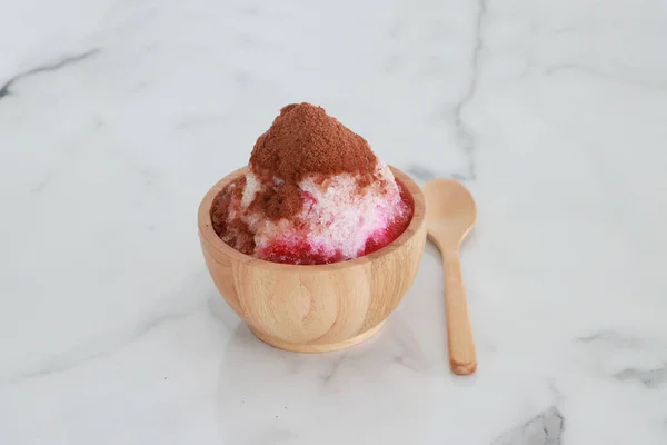 crushed ice Or shaved ice with sweet red water and sweetened condensed milk, Topped with chocolate powder, looks like a volcano. in a round wooden bowl with wooden spoon. It is a dessert that is refreshing to eat.