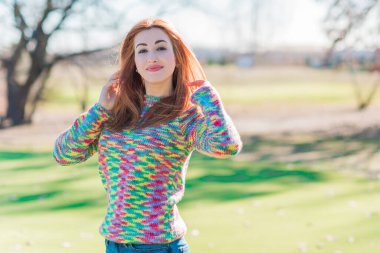 Yün ceketli bir kadın, renkli bir kazak, şehir parkında güzel bir kadının portresi, modaya uygun bir konsept.