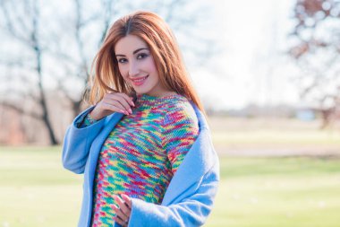 Yün ceketli bir kadın, renkli bir kazak, şehir parkında güzel bir kadının portresi, modaya uygun bir konsept.