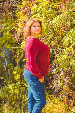 Şehir parkında, tombul, güneşli, sıcacık elbiseli bir kadın. Büyük bedenli bayanlar için kıyafetler.