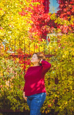 Şehir parkında, tombul, güneşli, sıcacık elbiseli bir kadın. Büyük bedenli bayanlar için kıyafetler.