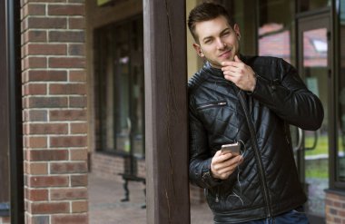 İlginç bir genç adam mavi kot pantolon, siyah ceket, şık saç, iyi ruh hali, telefon, güzel moda erkek arkadaş, vatandaş, yalnız, güzel yüzlü.