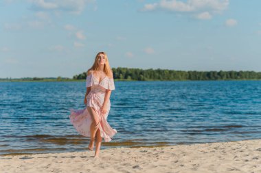 Plajda pembe romantik, yumuşak, uzun elbiseli bir kadın, güneşli sıcak bir gün. Rahatla ve özgürlük kavramı 