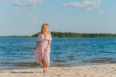 Plajda pembe romantik, yumuşak, uzun elbiseli bir kadın, güneşli sıcak bir gün. Rahatla ve özgürlük kavramı 