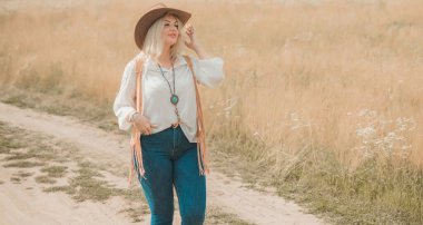 Woman Plus size in American country style black boho jacket, with a fringe, shirt and cowboy hat at nature