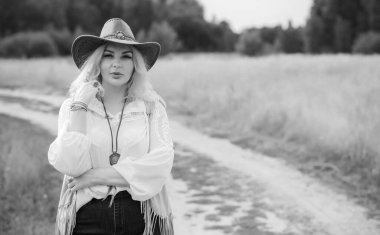 Woman Plus size in American country style black boho jacket, with a fringe, shirt and cowboy hat at nature