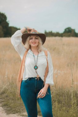 Woman Plus size in American country style black boho jacket, with a fringe, shirt and cowboy hat at nature