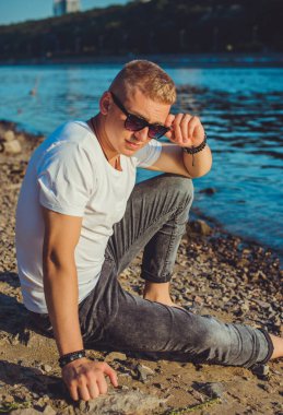 Young guy at beach in tranquility mood, rest in vacation. Summer portrait of handsome men at beach, concept of vacation, rest time 