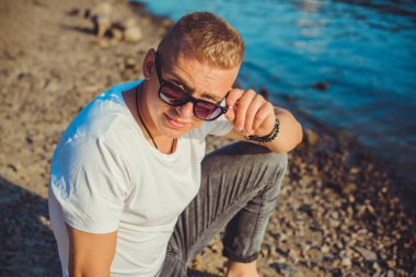 Young guy at beach in tranquility mood, rest in vacation. Summer portrait of handsome men at beach, concept of vacation, rest time 