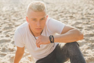 Young guy at beach in tranquility mood, rest in vacation. Summer portrait of handsome men at beach, concept of vacation, rest time 