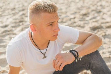 Young guy at beach in tranquility mood, rest in vacation. Summer portrait of handsome men at beach, concept of vacation, rest time 