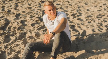 Young guy at beach in tranquility mood, rest in vacation. Summer portrait of handsome men at beach, concept of vacation, rest time 