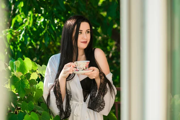 Femininity sexy woman on a balcony with a cup of tea, concept of tenderness and ladies sensuality