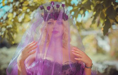 Pembe korseli Cadılar Bayramı gelini, gotik çiçekli çelenk ve doğa arka planında peçe, parti için kıyafetler.