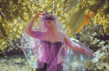 Pembe korseli Cadılar Bayramı gelini, gotik çiçekli çelenk ve doğa arka planında peçe, parti için kıyafetler.