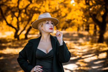 Sonbahar havası konsepti. Sonbahar bahçesinde şık, neşeli sarışın bir kadın. Güzel aksesuarlı ve doğal bir tarzı olan bir bayan.