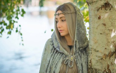 İskandinav konsepti, eski dünya büyüsü, İskandinav konsepti, İskandinav tarzı uzun sarı saçlı, elf, gri mantolu fantezi kadın. Cadılar Bayramı kostümü