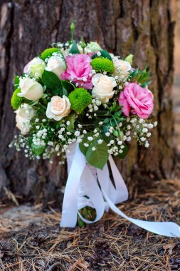 Çam ağacının altındaki bir ormanda pembe, krema ve yeşil çiçek buketi..