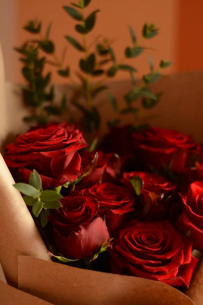 在橘红色背景的牛皮纸上 有一束郁郁葱葱的美丽红玫瑰 花关闭了 一个浪漫的节日礼物 — 图库照片