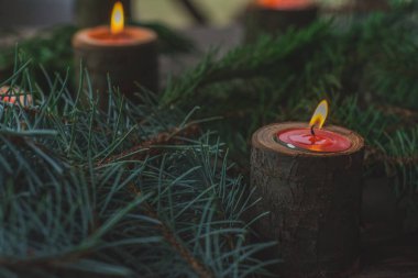 Noel ağacının yeşil dalları ve thuja arasında tahta şamdanlarda mumlar. Rahatlamak ve dinlenmek için atmosfer. Kırmızı mumlar ve tabletler yanıyor. Düğün, Sevgililer Günü ya da kilise dekorasyonu..