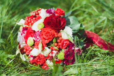 Parlak renkli gelin buketi, kırmızı, bordo ve beyaz güllerden oluşan çiçekleri ve yeşil çimlerin üzerine yeşil bir kurdele ile bağlanmış kırmızı viburum çilekleri.. 