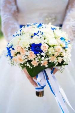 Beyaz ve kremalı güllerden oluşan narin bir gelin buketi, mavi kasımpatılar ve beyaz gelinliğin arka planında beyaz çiçekler. Özel durumlar için çiçekler. Aşkın Tatili.