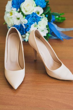 Krem renkli gelinin düğün ayakkabıları ahşap bir yüzeye yakın plan üzerinde beyaz güller, papatyalar ve cyan kurdeleli mavi kasımpatılar..