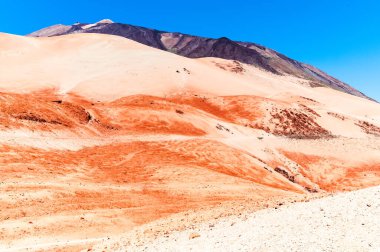 Kırmızı ve mavinin tonlarında katmanlar. Volkanın eteğinde terk edilmiş bir bölge. Teide zirvesi