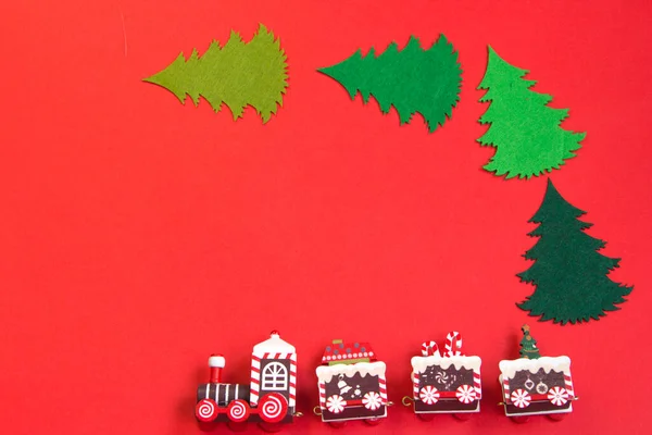 Kırmızı arka planda yeni yıl planı, eldivenler, kızak, ahşap yeni yıl treni, ahşap Noel ağaçları. 2022